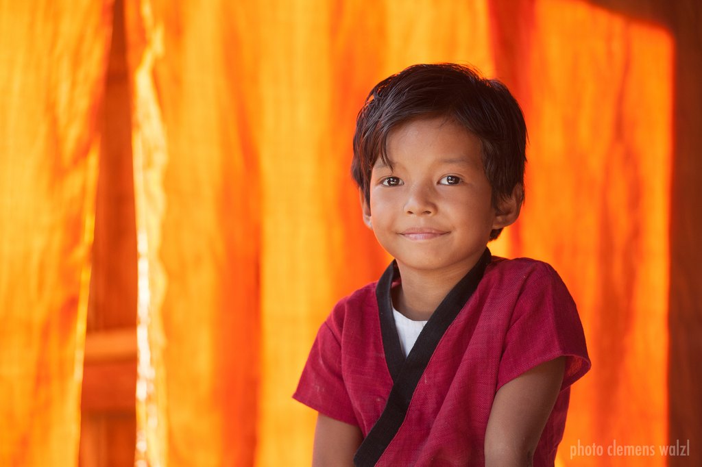 Porträt eines lächelnden Jungen vor orangefarbenem Hintergrund, Myanmar